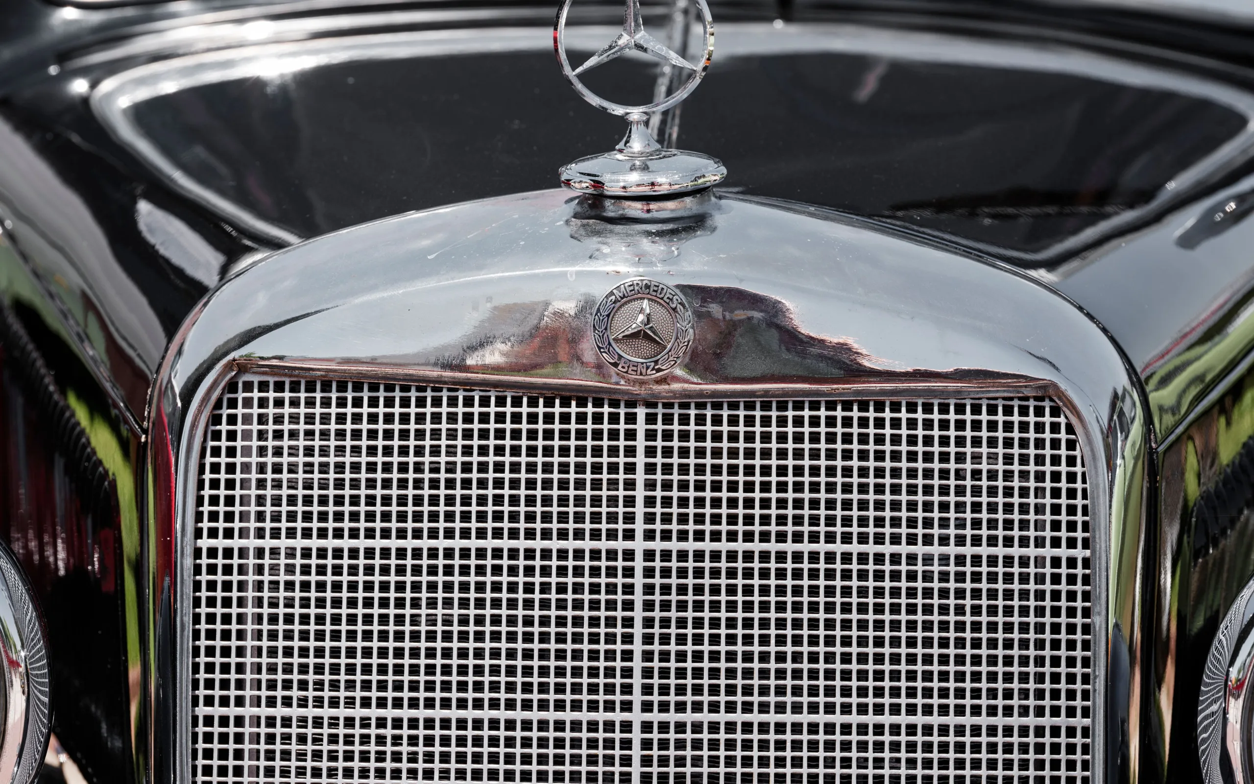 Façade d’une calandre de voiture avec emblème central : logo circulaire monté sur la grille et reflets de carrosserie au sol.